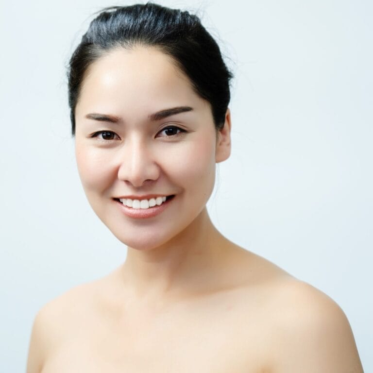 Smiling individual with dark hair pulled back, showcasing a clear complexion. Visiting YOLOve Beauty Spa in Dartmouth promises rejuvenation and tranquility. Enjoy personalized treatments in a serene environment, enhancing your natural beauty and leaving you radiant and relaxed.