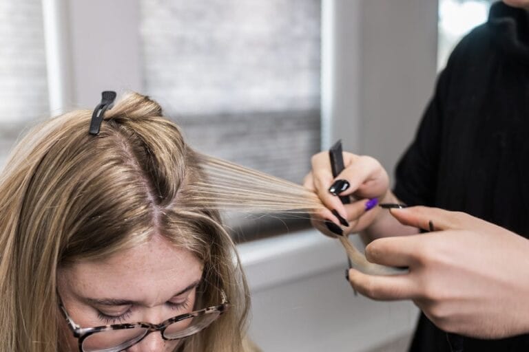 A stylist at YOLOve Beauty Spa in Dartmouth expertly parts and styles a client's long blonde hair, using a comb near a sunlit window.